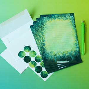 May include: Stationery set featuring a stack of lined notepaper with a green and yellow floral border, a green pen, white envelopes, and a sheet of green circle stickers. The stationery has a nature-inspired theme.