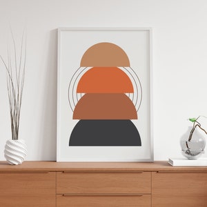 May include: A framed print with an abstract design featuring four stacked semi-circles in shades of orange, brown, and black. The background is white.