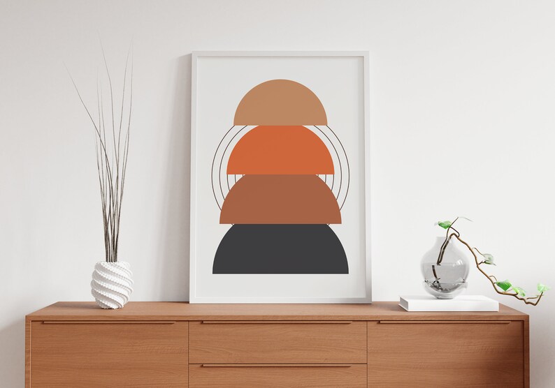 May include: A framed print with an abstract design featuring four stacked semi-circles in shades of orange, brown, and black. The background is white.
