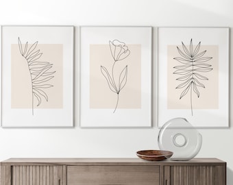 Puede incluir: Tres impresiones enmarcadas con dibujos minimalistas de plantas en líneas sobre un fondo beige. Las impresiones están colgadas en una pared blanca sobre un gabinete de madera.
