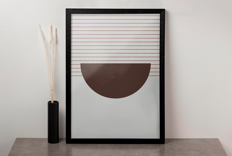 May include: A framed print with a minimalist design featuring a brown half-circle shape against a white background with thin horizontal lines.