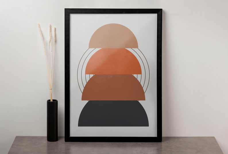 May include: A framed print with an abstract design featuring three stacked semi-circles in shades of brown, orange, and black. The semi-circles are layered on top of each other, creating a geometric pattern.