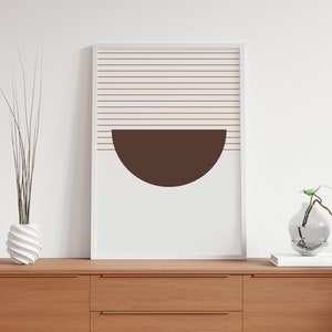 May include: A white framed print with a brown half-circle shape and thin horizontal lines in a light brown color. The print is hanging on a white wall above a wooden dresser with two drawers.