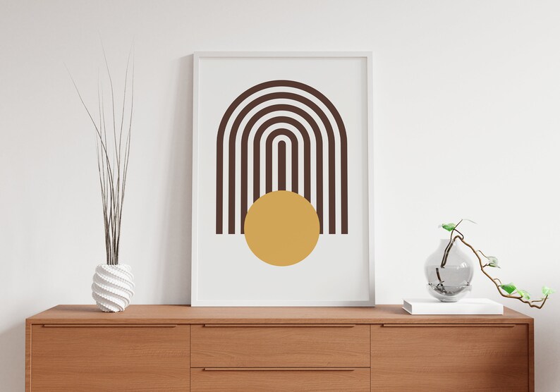 May include: A framed print with a minimalist design featuring a brown and white striped arch shape with a yellow circle in the center.