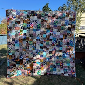May include: A large rectangular quilt constructed from a multitude of small, square fabric patches in a diverse array of colors, patterns, and textures. The patchwork design features various floral, geometric, and abstract prints stitched together.