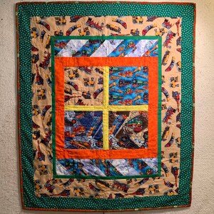 May include: A patchwork quilt with a green border and a beige background. The quilt features a repeating pattern of small trains in various colors. The center of the quilt is divided into nine squares, each with a different train design.