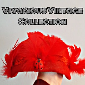 以下が含まれることがあります： 赤い羽根の帽子にテントウムシの装飾が施されています。帽子は人が被っていますが、顔は見えません。帽子はヴィンテージコレクションの一部です。