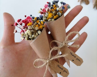 May include: Two small bouquets of dried baby's breath flowers in shades of pink, yellow, blue, and white, each wrapped in a brown paper cone. A jute twine bow secures each cone, featuring a small brown tag with the text Thank you... and a heart.