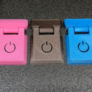May include: Three small plastic toggle switches, one pink, one brown, and one blue. Each switch has a raised power button symbol.