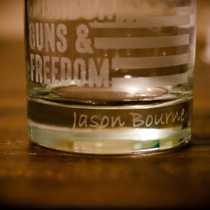 May include: A clear glass tumbler with the words "Guns & Freedom" etched on the side. The bottom of the glass has the name "Jason Bourne" etched into it.