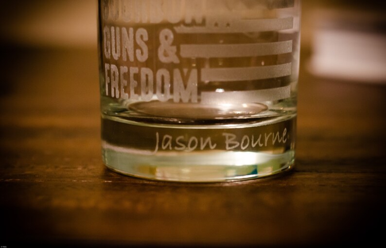 May include: A clear glass tumbler with the words "Guns & Freedom" etched on the side. The bottom of the glass has the name "Jason Bourne" etched into it.