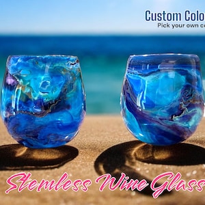 May include: Two blue and purple stainless steel wine glasses with a marbled design, sitting on a sandy beach with the text "Custom Colors!! Pick your own colors!" and "Stainless Wine Glass" on the image.