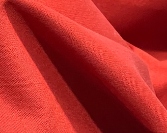 May include: Close-up of a red fabric with a textured surface. The fabric is folded and has a soft, smooth feel.