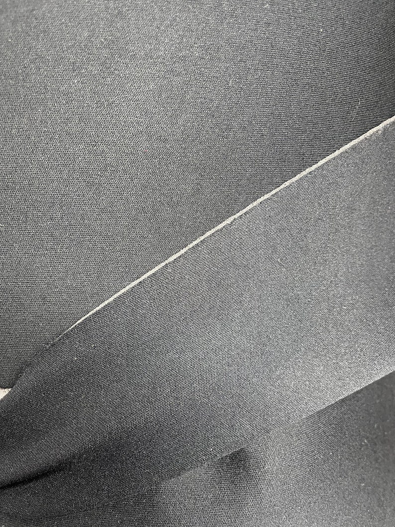 Puede incluir: Primer plano de tela negra con una textura sutil. La tela est&aacute; doblada, creando una costura.