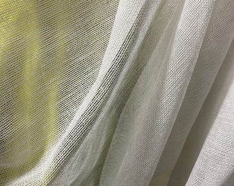 Op de afbeelding: Witte, doorschijnende gordijnstof met een fijne maasweefsel. De stof is gedrapeerd en gevouwen, waardoor een zachte, vloeiende textuur ontstaat.