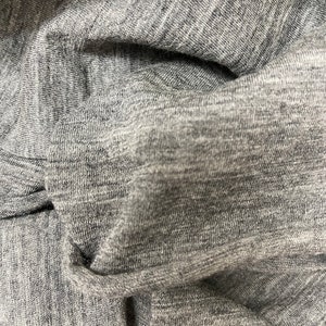 May include: Close-up of a gray, textured fabric with a subtle sheen. The fabric is folded and wrinkled, showing its soft and drapey nature.