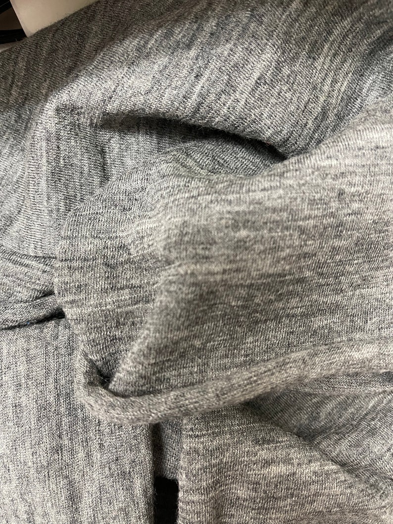 May include: Close-up of a gray, textured fabric with a subtle sheen. The fabric is folded and wrinkled, showing its soft and drapey nature.