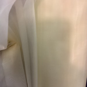 Può includere: Due pezzi di tessuto trasparente, uno bianco e uno avorio, sono piegati insieme. Il tessuto è morbido e delicato, con un leggero luccichio.