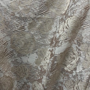 May include: A close-up of a textured fabric with a white and brown pattern. The fabric has a subtle sheen and a slightly wrinkled appearance.