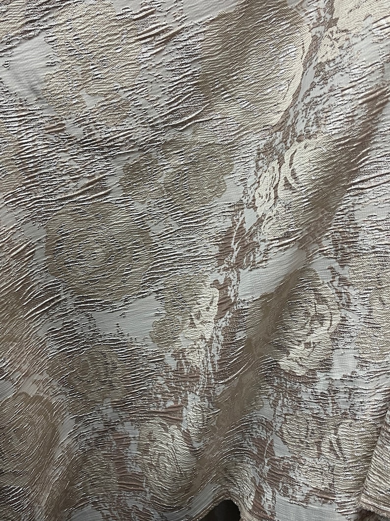 May include: A close-up of a textured fabric with a white and brown pattern. The fabric has a subtle sheen and a slightly wrinkled appearance.