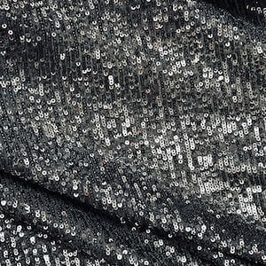 May include: Close-up of a fabric covered in small, reflective, silver and black sequins. The sequins are densely packed and create a shimmering effect. The fabric is slightly draped, showing the texture and movement of the material.