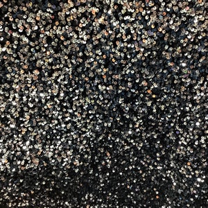 May include: A close-up of a fabric covered in iridescent sequins. The sequins are a mix of black, silver, and gold.