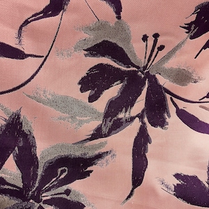 Könnte beinhalten: Ein rosa Stoff mit einem Blumenmuster. Die Blumen sind dunkelviolett und silberfarben mit einem Pinselstrich-Effekt.
