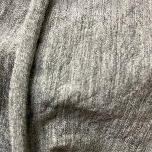 May include: Close-up of a gray, textured fabric with a subtle sheen. The fabric is soft and has a slightly wrinkled appearance.