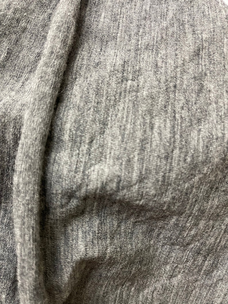 May include: Close-up of a gray, textured fabric with a subtle sheen. The fabric is soft and has a slightly wrinkled appearance.