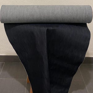 May include: A rolled-up gray fabric sits atop a draped black fabric. The fabrics appear to be a heavy weight, possibly for upholstery or other home decor projects. The image is taken indoors.