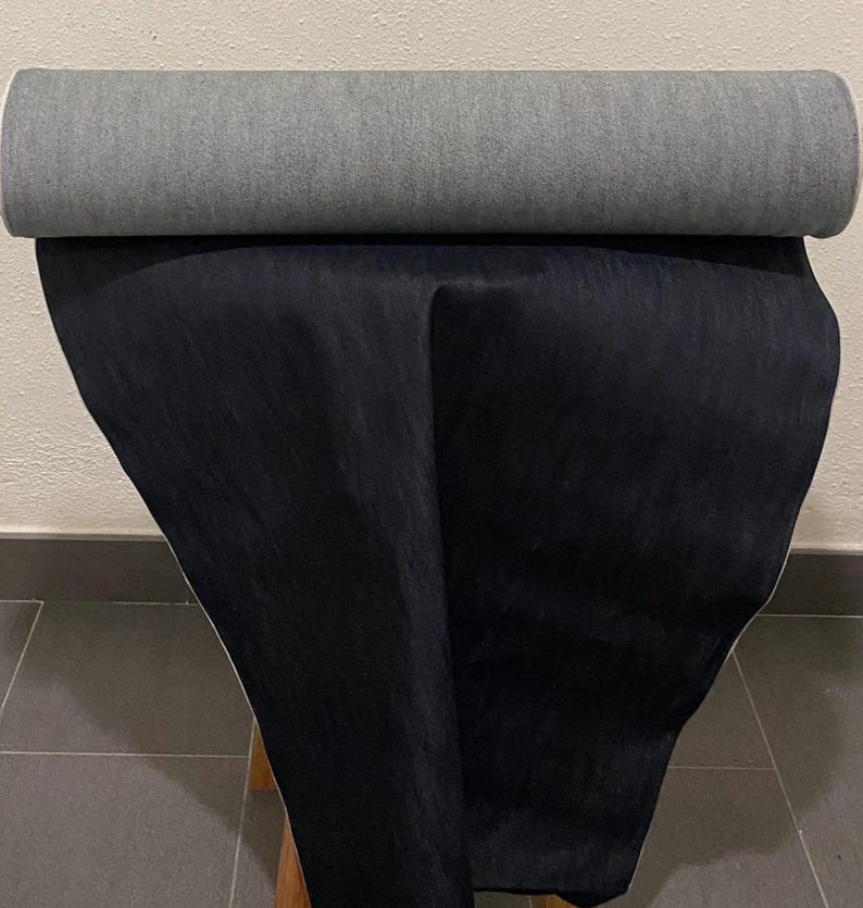 May include: A rolled-up gray fabric sits atop a draped black fabric. The fabrics appear to be a heavy weight, possibly for upholstery or other home decor projects. The image is taken indoors.