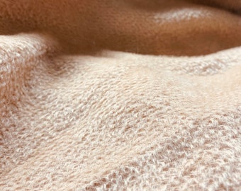 May include: Close-up of a soft, beige, fuzzy fabric with a textured weave.