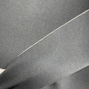 Puede incluir: Primer plano de una tela negra con una textura sutil. La tela est&aacute; doblada por la mitad, creando una costura diagonal.