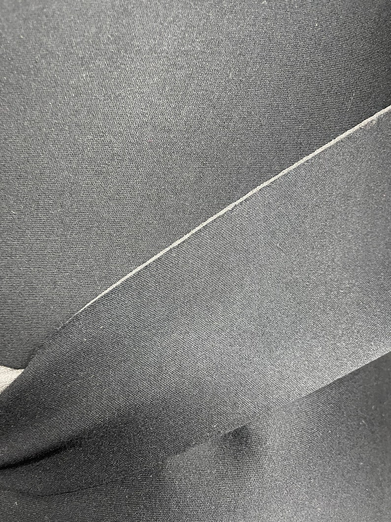 Puede incluir: Primer plano de una tela negra con una textura sutil. La tela est&aacute; doblada por la mitad, creando una costura diagonal.