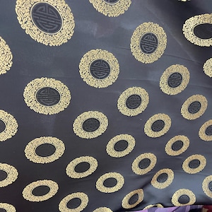 May include: Black fabric with a repeating pattern of gold oval-shaped designs. Each design features a stylized Chinese character in the center.
