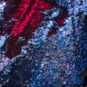 Könnte beinhalten: Nahaufnahme eines Stoffes mit Wendepailletten. Die Pailletten wechseln zwischen Rot und Blau und erzeugen einen schimmernden Effekt. Die Textur des Stoffes ist sichtbar, wobei jede Paillette Licht reflektiert.