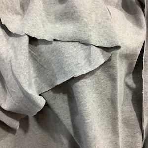 May include: Gray fabric with a textured surface. The fabric is folded and draped, creating a soft and flowing look.