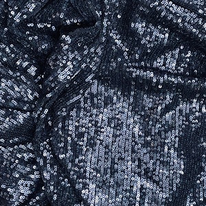 May include: Close-up of a dark blue fabric covered in silver sequins. The sequins are arranged in a repeating pattern.