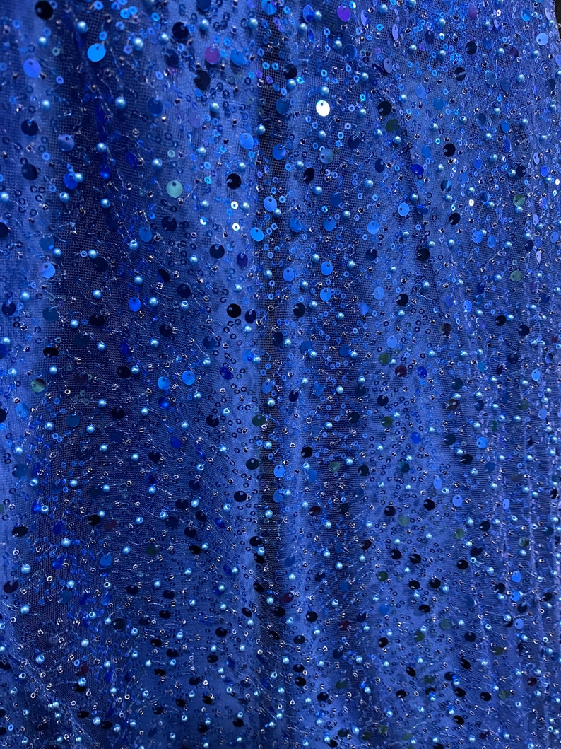 May include: Close-up of a blue fabric with small sequins and beads. The fabric has a shimmery, iridescent look.