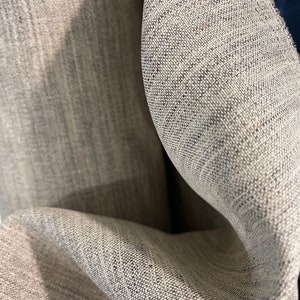 Puede incluir: Primer plano de una tela gris texturizada con un sutil patrón tejido. La tela está doblada y drapeada, mostrando su textura suave y fluida.