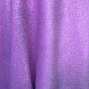 May include: A close-up of a soft, purple fabric with a textured surface. The fabric is folded and draped, creating a smooth, flowing look.
