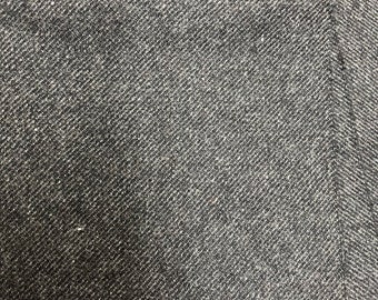 May include: Close-up of a dark gray fabric with a diagonal weave pattern. The fabric has a pocket sewn into it.