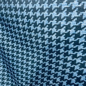May include: Close-up of a fabric with a houndstooth pattern. The pattern features a repeating design of black and light blue shapes. The fabric appears to be soft and has a slight sheen, suggesting it could be used for clothing or home decor.