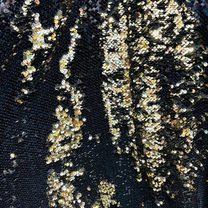 May include: Close-up of a black fabric with gold sequins. The sequins are arranged in a pattern that resembles scales.