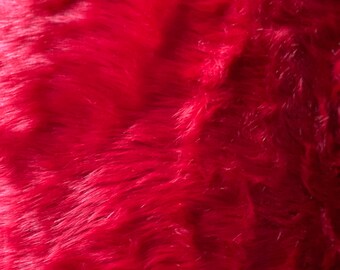 Può includere: Primo piano di un tessuto in pelliccia sintetica rosso scuro. La pelliccia è morbida e soffice, con un aspetto leggermente strutturato.
