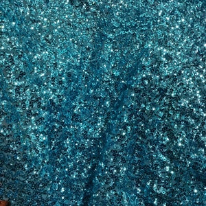 May include: A close-up of a turquoise fabric covered in sequins. The sequins are small and densely packed, creating a shimmering effect.
