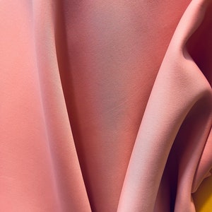 May include: A close-up of a soft, peach-colored fabric with a smooth texture. The fabric is draped and folded, creating a soft, flowing look.