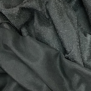 Può includere: Tessuto nero trasparente con una superficie testurizzata. Il tessuto è piegato e drappeggiato, mostrando la texture e il drappeggio del materiale.