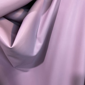 K&ouml;nnte beinhalten: Nahaufnahme eines weichen, glatten, helllila Stoffes. Der Stoff ist gefaltet und drapiert, wodurch seine Textur und Farbe sichtbar werden.