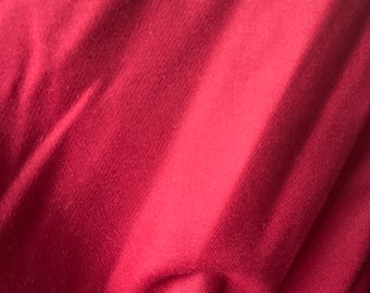 May include: Close-up of a deep red fabric with visible folds and shadows. The texture appears soft and possibly woven, with a subtle sheen. The fabric's color is consistent throughout the image.